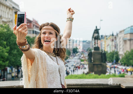 Happy young brunette bohemian woman tourist making selfie in the historical center of Prague. In the background Saint Wenceslas Stock Photo
