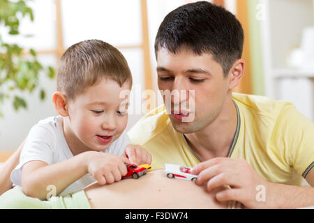 Cheerful father and son have a fun playing with toy car on pregnant wife belly. Stock Photo