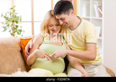 Happy couple pending baby.  Smiling man embraces his pregnant woman looking at her belly. Stock Photo