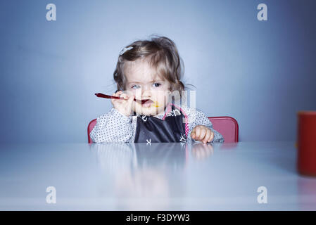 Baby girl sitting at table, eating with spoon Stock Photo