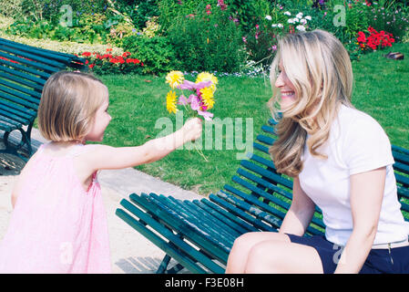 Little girl giving her mother a bouquet of flowers in park Stock Photo