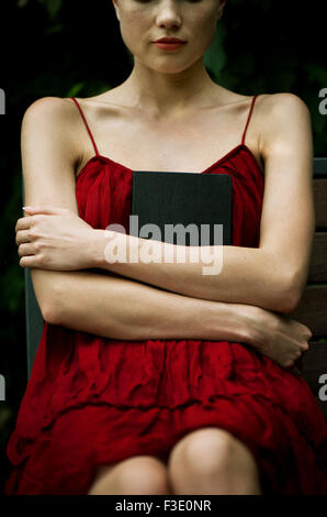 Young woman sitting with arms folded across chest, holding book protectively Stock Photo