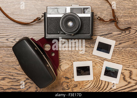 Old film camera with leather case and slides on a wooden floor. Stock Photo