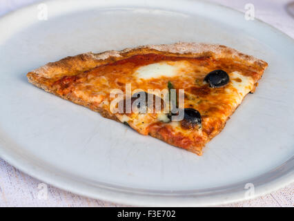 In the picture a slice of pizza with tomato, mozzarella cheese and olives served on a white dish at the restaurant. Stock Photo