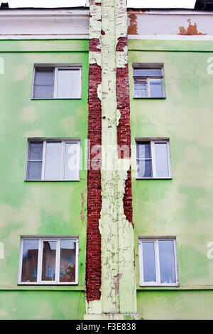 Green cracked plaster on red brick house with windows. Bottom view Stock Photo