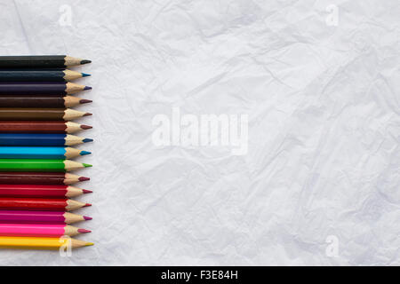 Colored pencils in a row on crumpled white sheet of paper Stock Photo