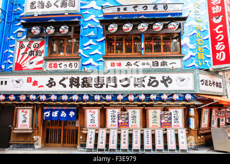 Osaka, Shinsekai. Famous puffer fish restaurant, Zuboraya. Exterior of building covered in blue and white signs and chochin paper lanterns. Stock Photo