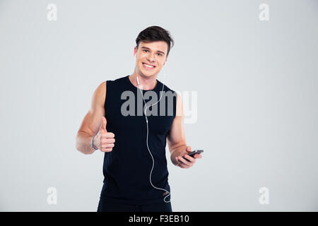 Portrait of a happy sports man holding smartphone with headphones and showing thumb up isolated on a white background Stock Photo