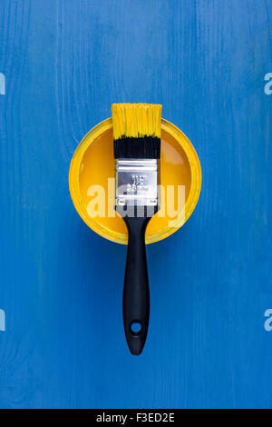 Pot of Yellow paint and brush on a blue wooden background Stock Photo