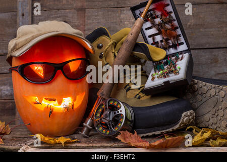 halloween pumpkin head with wading boots and fly-fishing tackles on wooden boards background Stock Photo