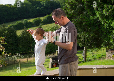 Father helping 16 month old baby girl to walk Stock Photo