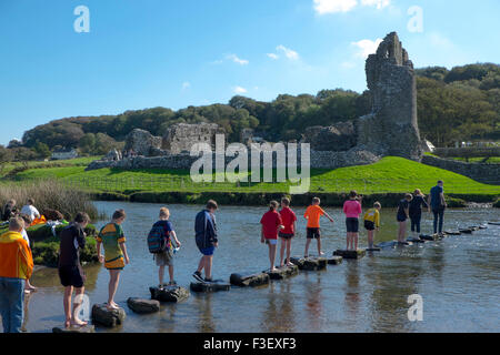 Children using stepping stones to cross the River Ogmore near Ogmore Castle, South Glamorgan, South Wales,UK Stock Photo