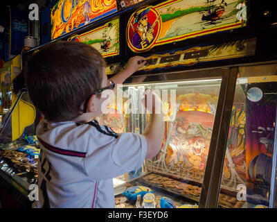 A very young boy plays on a gambling machine in a penny amusement arcade Stock Photo