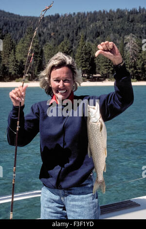 A young woman proudly displays the Lake Trout (Salvelinus namaycush) she caught while fishing in Lake Tahoe, North America's largest alpine lake. It is located in the Sierra Nevada mountains along the border of California and Nevada, USA. The freshwater lake also is the second deepest in the nation (after Crater Lake in Oregon) and home to other popular game fish including Kokanee Salmon, Rainbow Trout and Brown Trout. Mackinaw is the local name for Lake Trout. Model released. Stock Photo