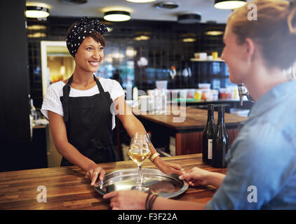 Cheerful Waitress Serving Glasses of Wine on a Silver Tray to a Female Customer inside the Pub. Stock Photo