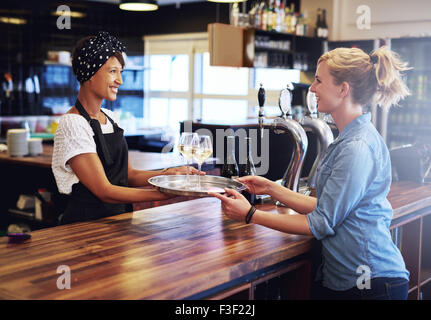 Smiling Waitress Giving Glasses of Wines on a Tray to a Female Customer at the Bar Counter. Stock Photo