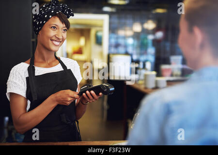 Smiling attractive African American small business owner taking payment from a customer processing a credit card through the han Stock Photo