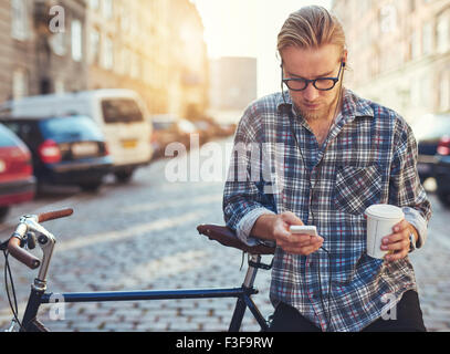 Outdoor portrait of modern young man with mobile phone in the street, sitting on bike Stock Photo