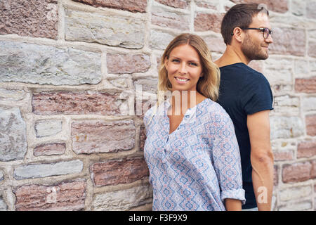 Couple standing back against each other against a wall Stock Photo