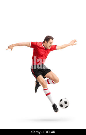 Full length portrait of a young football player in red jersey kicking a ball in mid-air isolated on white background Stock Photo