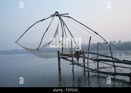 Fisherman standing on platform of Chinese net observing calm water