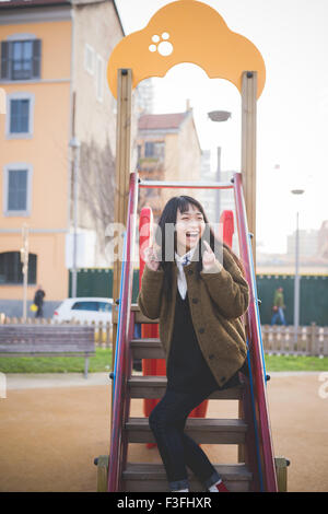 young beautiful asian long brown straight hair hipster woman playing in a recreation ground, overlooking left, laughing - childhood, youth, carefreeness concept Stock Photo