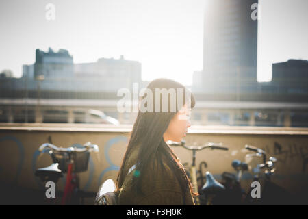 Portrait profile of young beautiful long brown straight hair asian hipster woman walking in the city during sunset in backlit - Stock Photo