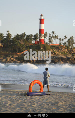 Kovalam beach and light house ; orange life guard ring with life guard watching waves ; ThiruvananthapuramDrict ;; India Stock Photo