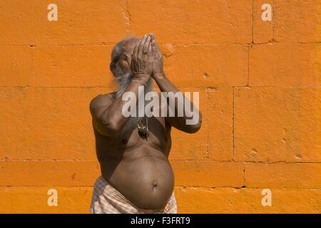 Hindu saint worshiping in Varanasi on orange background ; Uttar Pradesh ; India Stock Photo