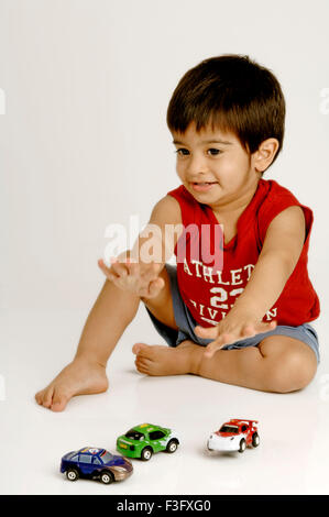 Indian Boy playing with various models of cars ; MR Stock Photo