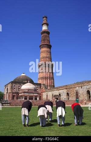 Children doing Namaz in front of Alai Darwaza Imam Zamin's tomb and Qutab Minar red sandstone tower ; Indo Muslim art Delhi Stock Photo