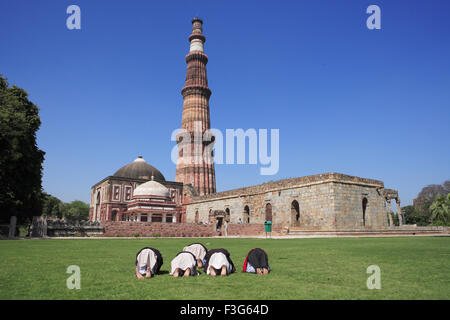 Children doing Namaz Alai Darwaza Imam Zamin tomb and Qutab Minar red sandstone tower Indo Muslim art Delhi Stock Photo