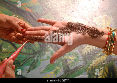 woman applying mehndi design on hand ; India ; Asia Stock Photo