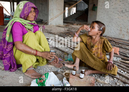A mother giving medicine to her sick daughter at a construction site during the lunch break ; Ahmedabad ; Gujarat ; India