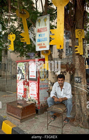 A duplicate key maker setting up his shop under a tree with a display of huge key cutouts to attract customers ; Mumbai Stock Photo