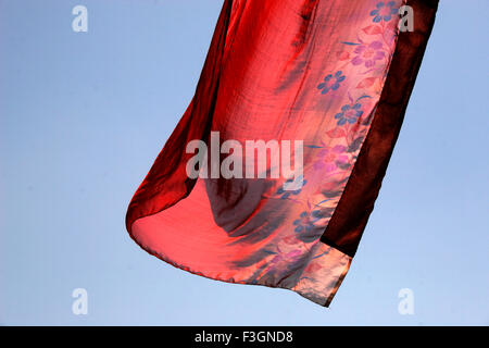 Abstract Indian traditional ladies wear saree red color flying air against blue skies wind while hanging drying after wash Pune Stock Photo