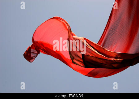 Abstract Indian traditional ladies wear saree red color flying in air against blue skies wind while hanging drying wash Pune Stock Photo