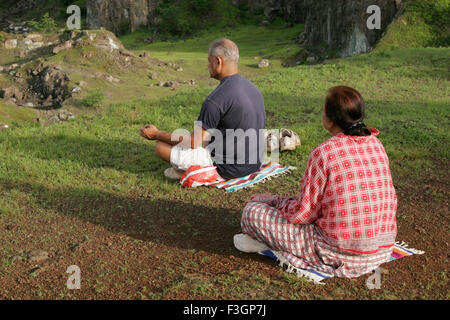 Middle aged couple sitting in fresh green open field in the morning and doing breathing exercise called 'Pranayam Stock Photo