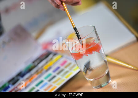 Artist's hand cleaning his brush in a glass of water Stock Photo