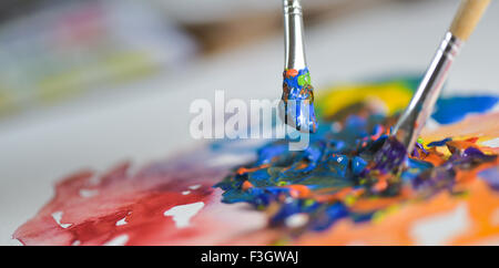 Brush mixing paint on palette-Artist's hand applying paint gouache on the drawing sheet Stock Photo