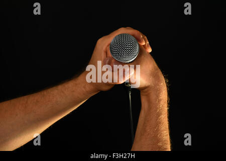 Two male hands holding microphone with wire cable isolated on black background Stock Photo