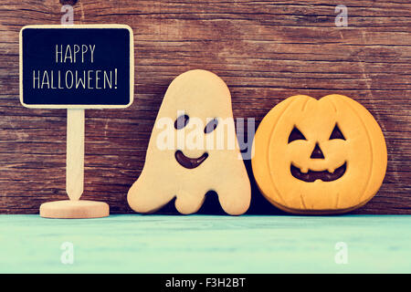 a chalkboard with the text happy halloween, a ghost-shaped cookie and a pumpkin-shaped cookie on rustic blue wooden surface Stock Photo