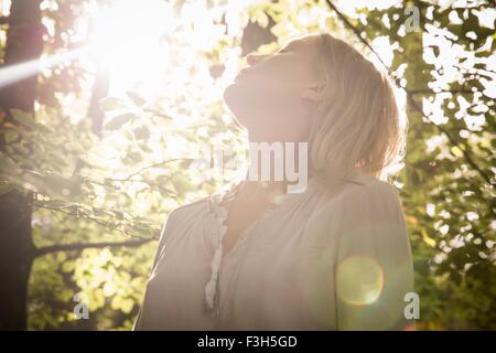 Mature woman standing in stream of light in forest Stock Photo