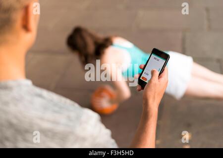 Over shoulder view of male trainer timing female runners push ups on smartphone Stock Photo