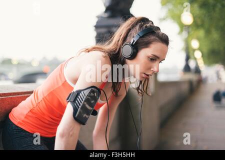 Exhausted female runner wearing headphones taking a break on riverside Stock Photo