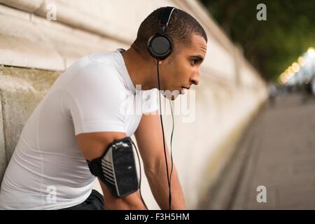 Exhausted male runner wearing headphones taking a break on riverside Stock Photo