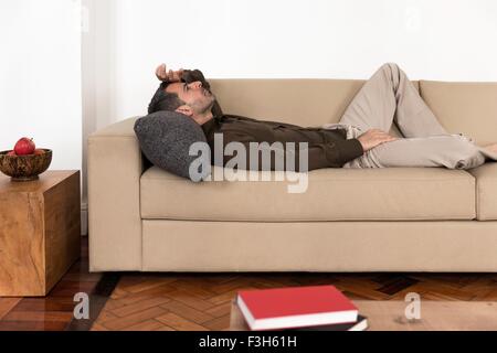 Side view of mature man lying on back on sofa hand on forehead, looking up Stock Photo