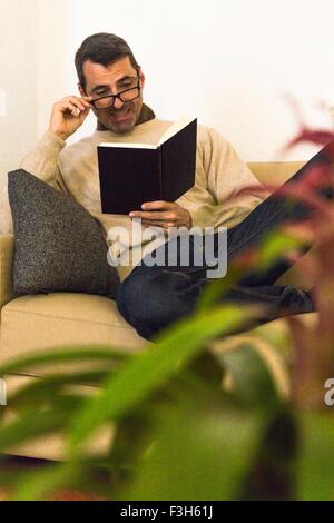 Mature man sitting on sofa wearing eye glasses reading a book Stock Photo