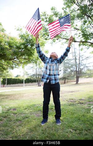 Boy holding up American flags in park Stock Photo