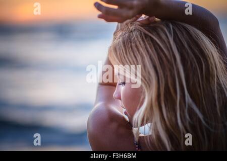 Young woman with arms raised on beach at sunset Stock Photo